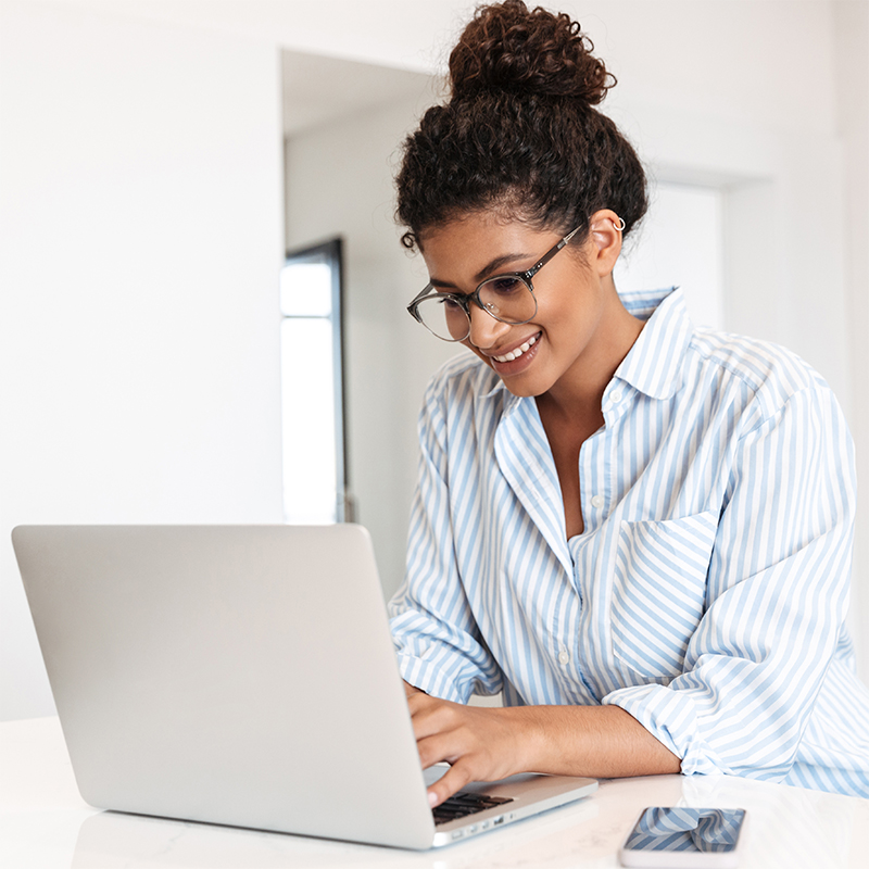 young woman wearing glasses browsing the internet on a silver laptop